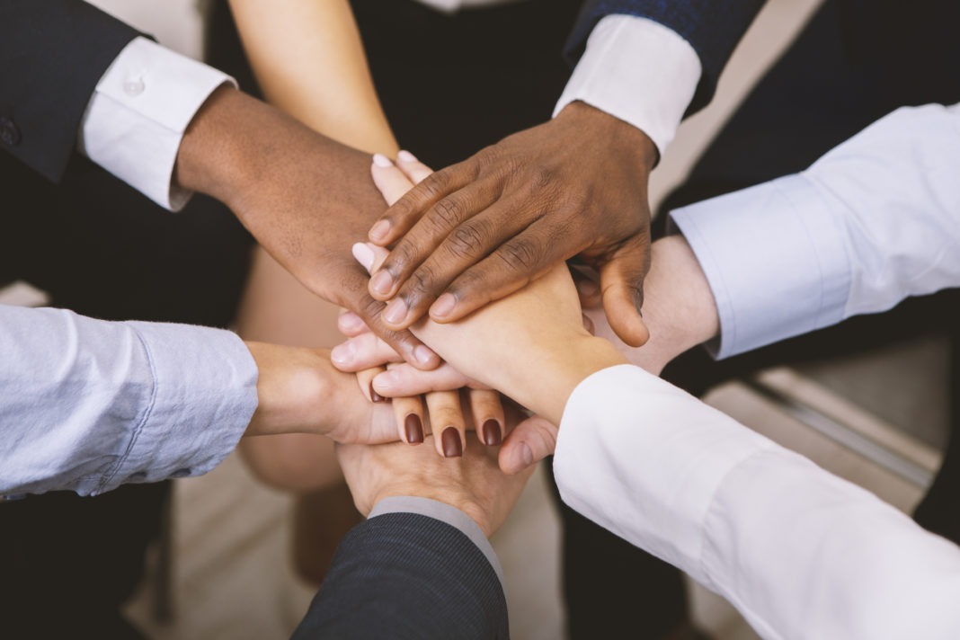 Multiethnic corporate teame stacking hands together in office DEI