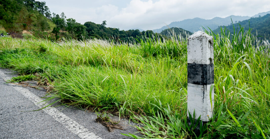 Black and white stones concrete pillar kilometers on the road are covered with grass. With a gray sky, rocky kilometers on the road are covered with grass. With a gray sky, rocky kilometers motivate