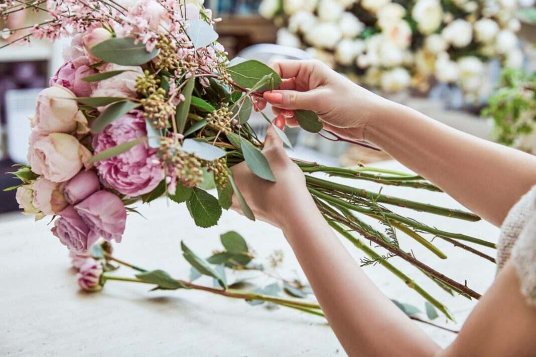 florist making bouquet of roses and peonies at workspace